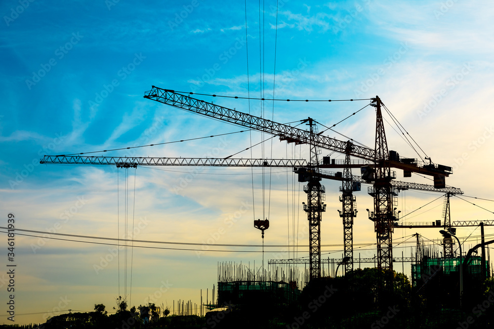 Tower crane and building construction site silhouette at sunrise.