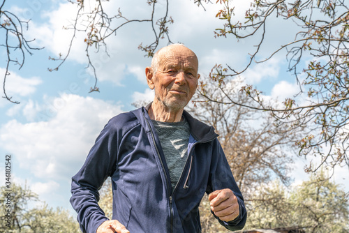 90 years old man in sportswear running among blooming garden during spring sunny day