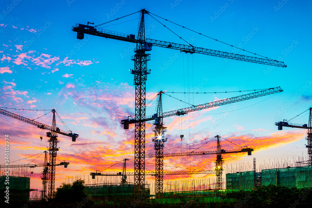 Tower crane and building construction site silhouette at sunrise.