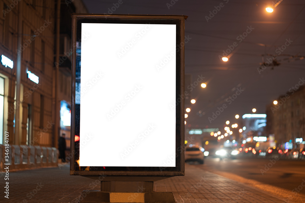 Advertising billboard vertical lightbox in the city at night glows, on the street near the road.