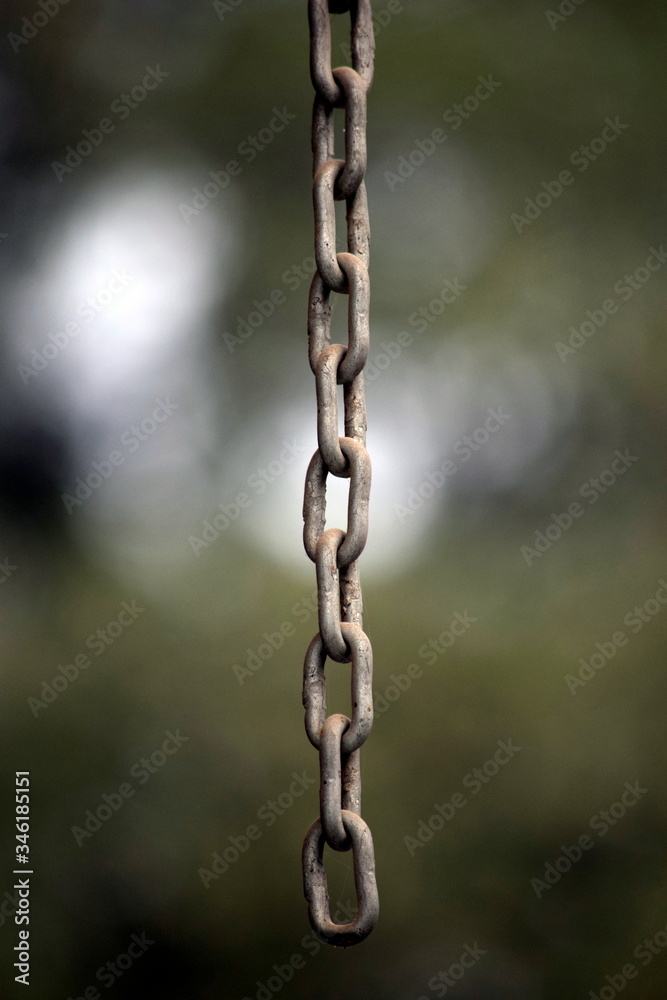 A rusted old chain, handing in the foreground with a strong blur in the background A rusted old chain, handing in the foreground with a strong blur in the background