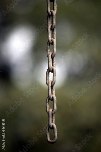 A rusted old chain, handing in the foreground with a strong blur in the background