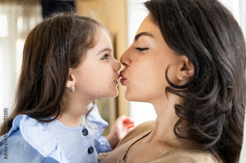 Friendly and loving family. Emotional portrait of a happy and cheerful little girl with her young mother kissing her on the lips.