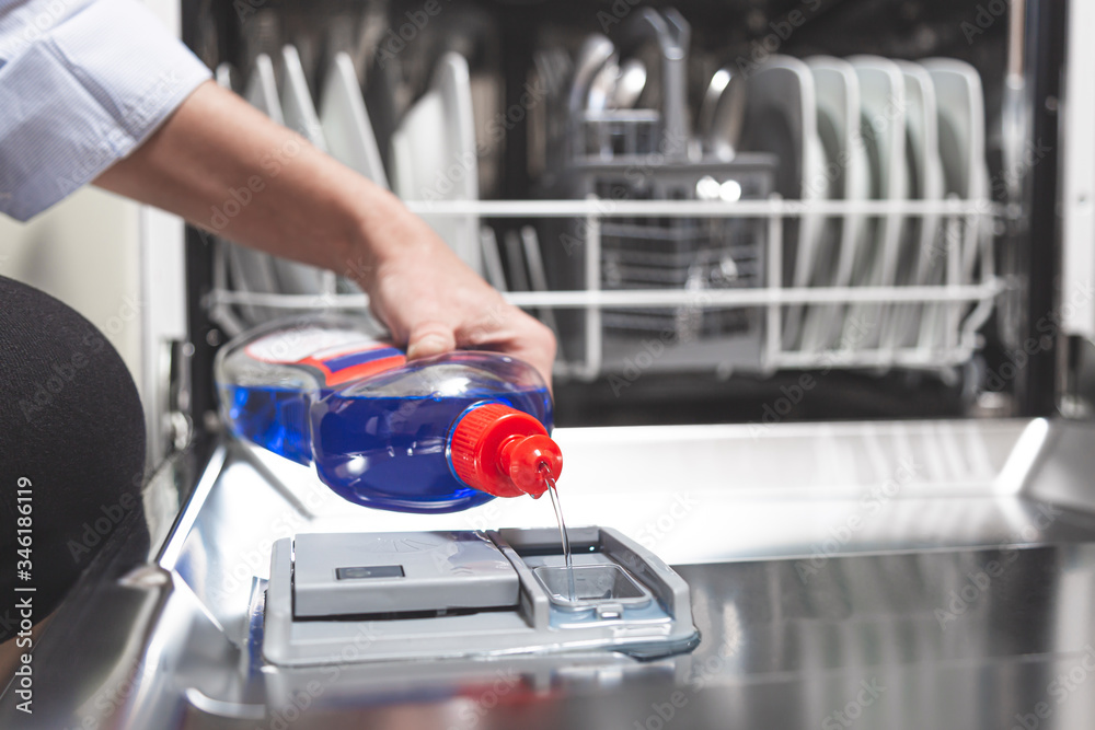 Close-up hand filling dishwasher with gloss liquid into the dishwasher box. Housework concept. Close-up hand filling dishwasher with gloss liquid into the dishwasher box. Housework concept.
