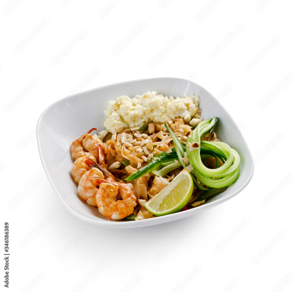 Fried udon noodles in a wok with shrimp and nuts. Served with fresh cucumber and lime. Traditional asian food. Isolated on a white background.