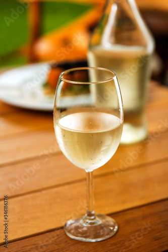 glass of white whine with condensation water drops bottle and meal in the background