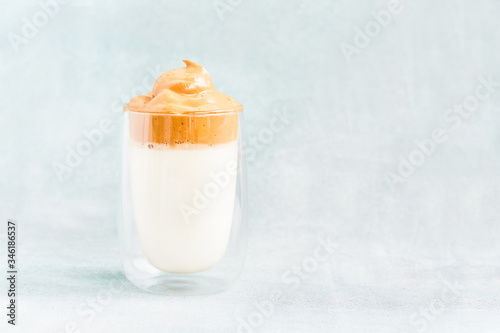 Trendy homemade Dalgona coffee in glass on blue background. Recipe of popular Korean drink latte with foam of instant coffee. DIY, instruction.