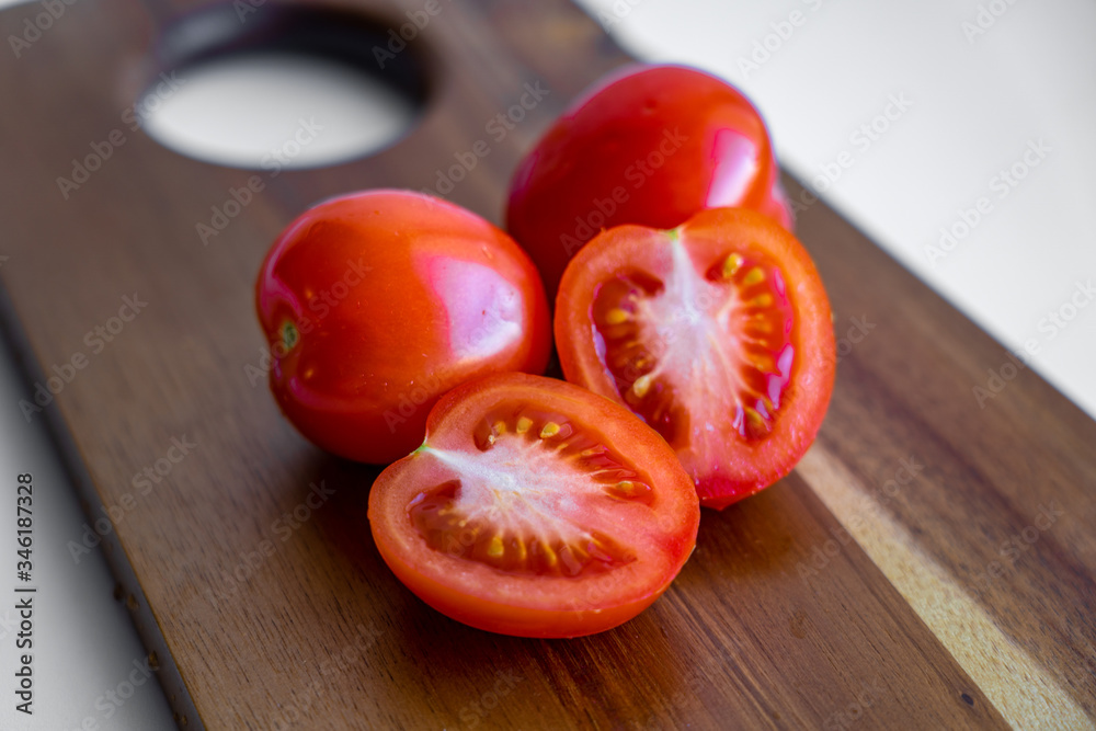 Two whole tomato and two halves of tomato isolated on a wooden cutting board on white background, closeup view Two whole tomato and two halves of tomato isolated on a wooden cutting board on white background, closeup view