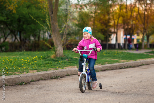 Beautiful 4-year-old girl in a pink jacket rides a bike in the spring © Botygin