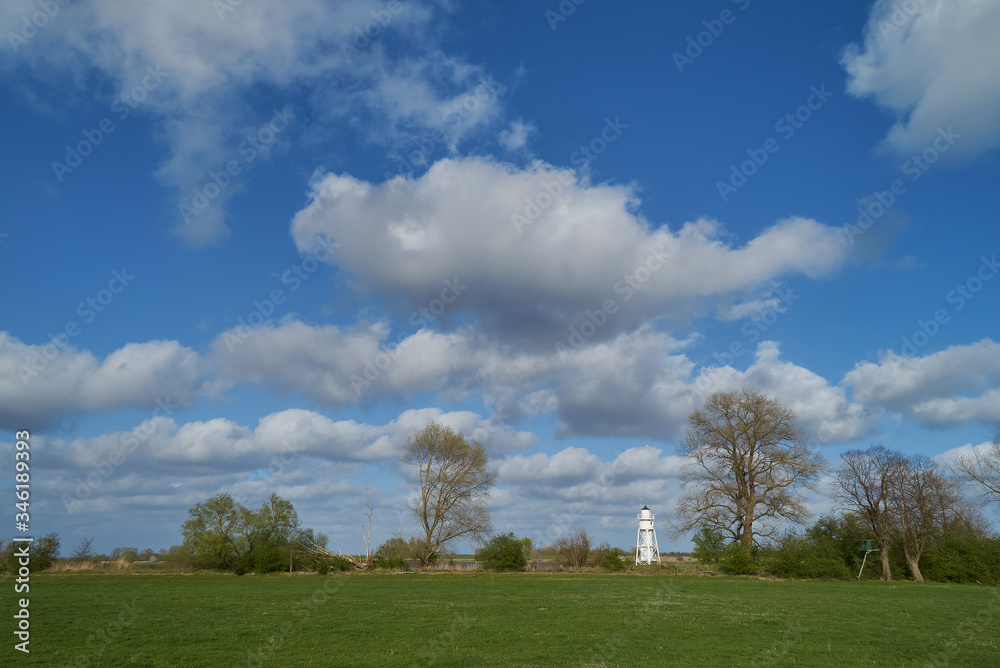 scenic white lighthouse on the island Elsflether Sand in the river Weser district Wesermarsch, Germany) seen far away at the horizon under vivid blue sky and white clouds scenic white lighthouse on the island Elsflether Sand in the river Weser district Wesermarsch, Germany) seen far away at the horizon under vivid blue sky and white clouds