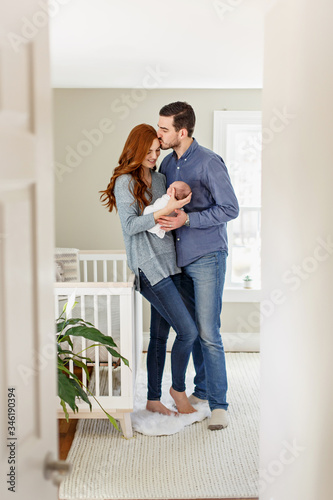 Dad kissing mom with a newborn in nursery.