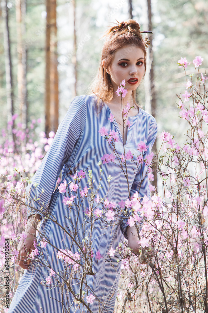 A girl dressed in Japanese style in a flowering forest among pink flowers A girl dressed in Japanese style in a flowering forest among pink flowers