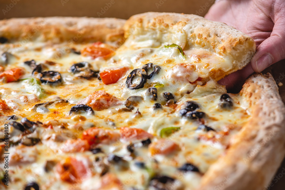 Slice of fresh hot vegetarian pizza with a stretch of mozzarella cheese in the cook's hand. Slice of fresh hot vegetarian pizza with a stretch of mozzarella cheese in the cook's hand.