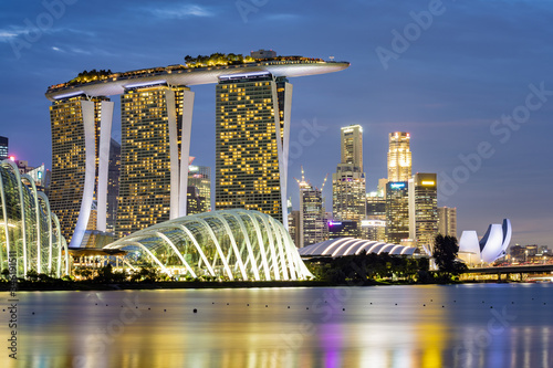 Stunning view of the illuminated skyline of Singapore at dusk with a calm bay in the foreground. Singapore is an island city-state of southern Malaysia.