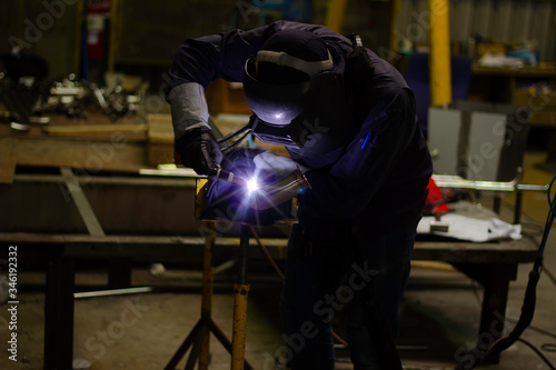 Welder is welding the steel in the factory. Weld the steel in dark. Workers wearing industrial uniforms and welding masks at a welding factory protect from welding sparks. Occupational safety concept