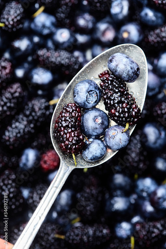 fresh mulberries and blueberries in spoon lifted from a big bowl of berries