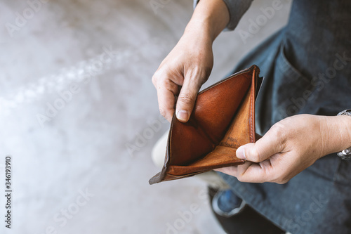closeup empty wallet (no money) in the hands of an man with soft-focus and over light in the background