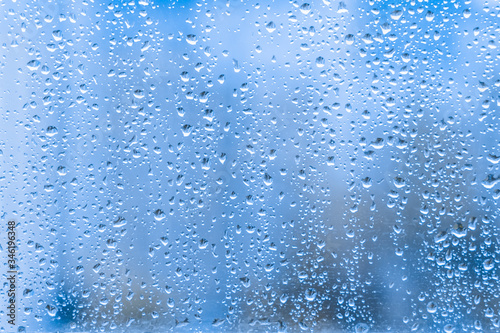 Close-up of water droplets on a light blue running down on glass transparent surface. rainy drops on a window pane during a summer shower stormy weather. rainy season.