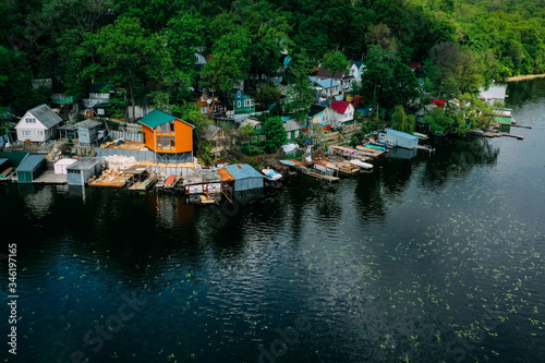 Russian fishing village with colored wooden houses and boats in a green oak forest on the river bank