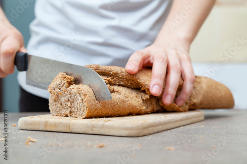 Whole grain bread on kitchen wood plate with a chef holding and cutting it. Fresh bread on the kitchen table. The healthy eating and traditional home made concept