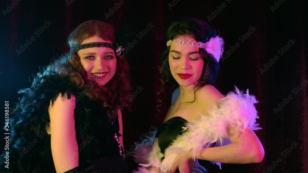 Attractive flappers women dressed in style of Roaring twenties posing on neon smoky background. Vintage, retro party, fashion, girls friends concept Attractive flappers women dressed in style of Roaring twenties posing on neon smoky background. Vintage, retro party, fashion, girls friends concept