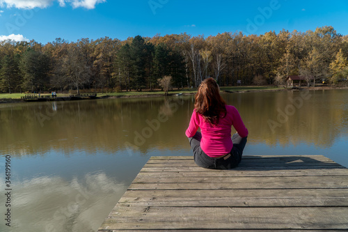 Girl sitting on a wooden bridge over the lake on a warm autumn day, photographed from the back © irinario