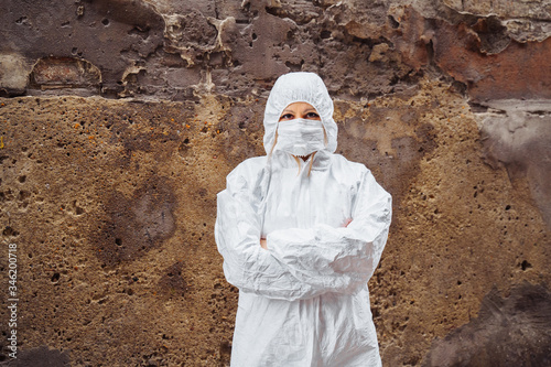 Фотография People's lives depend on doctors! Confident doctor, dressed in a white protective suit and protective mask, folded her arms over her chest