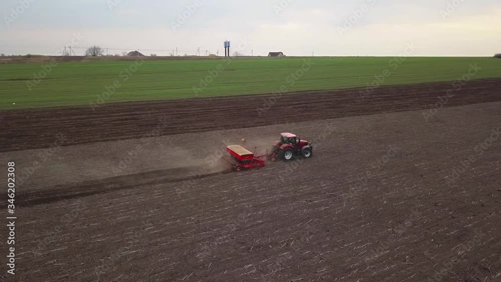 Aerial view of tractor with mounted seeder performing direct seeding of crops on plowed agricultural field. Technique for seeding crops at field. Sowing is the process of planting seeds in the ground.