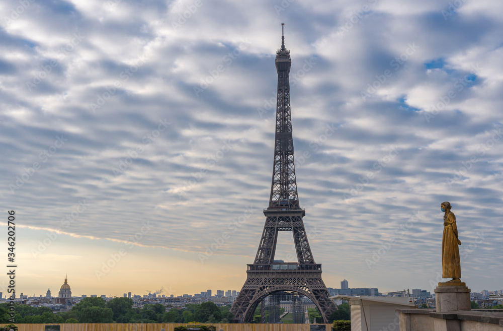 Paris, France - 05 06 2020: Golden statue of a woman wearing a surgical mask during confinement against coronavirus and the eiffel tower