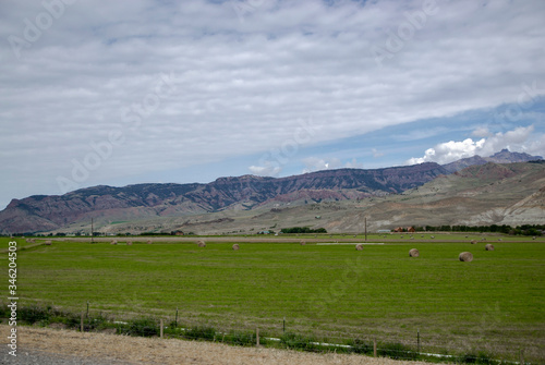 Green field with small hay bale there and mountains background cloudy sky with grey blue shade. Road to Yellowstone National Park in Wyoming state, picture for travel blog with copy space.