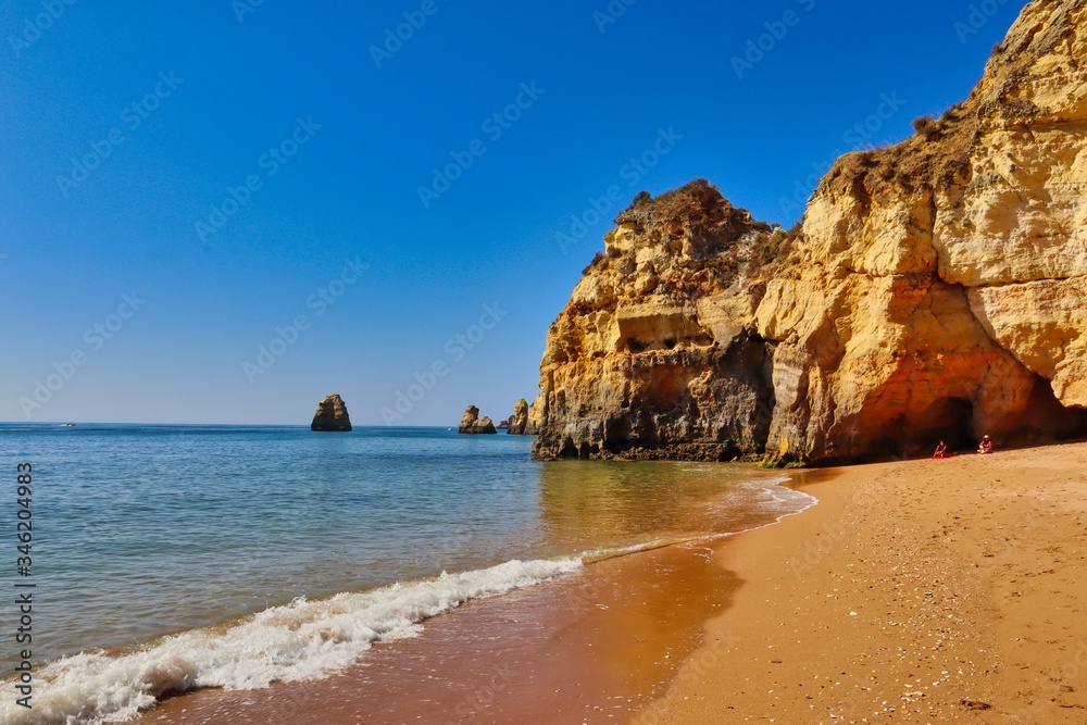 Cliff on Praia da Batata (Lagos, Portugal). Seashore picture with sand, cliff rock and blue sky.