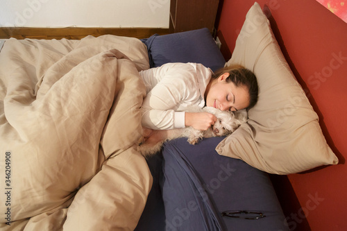 ragazza bianca dorme con affianco il proprio cane maltese nel letto a casa sua photo