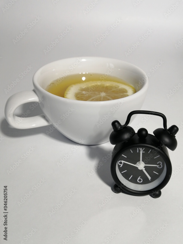 The watch is black next to a white Cup with green tea and lemon. Five o'clock. The watch is black next to a white Cup with green tea and lemon. Five o'clock.