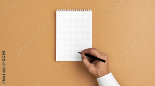 Męska ręka pisze w pustym notesie na jednolitym tle