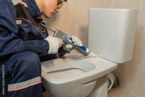 Worker using silicone or sealant to install the toilet bowl