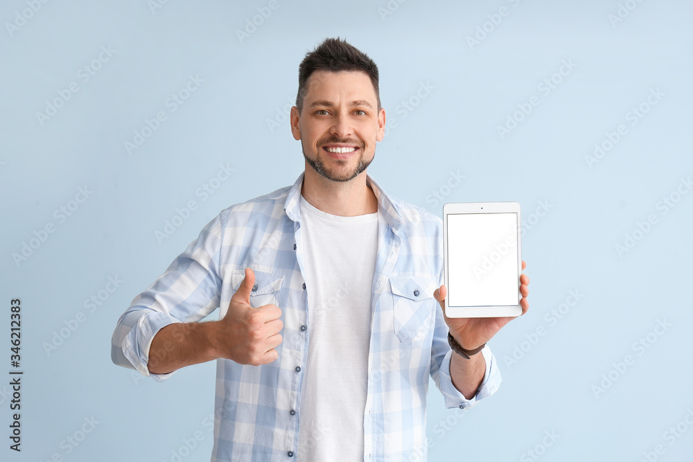 Handsome man with tablet computer showing thumb-up gesture on color background Handsome man with tablet computer showing thumb-up gesture on color background