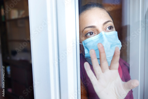 ragazza con la mascherina chirurgica guarda fuori dalla finestra attraverso un vetro con aria triste