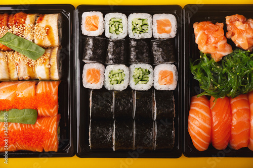 Sushi with fresh fish salmon and eel delivery in containers to the house on a bright yellow background. Top view, flat lay.