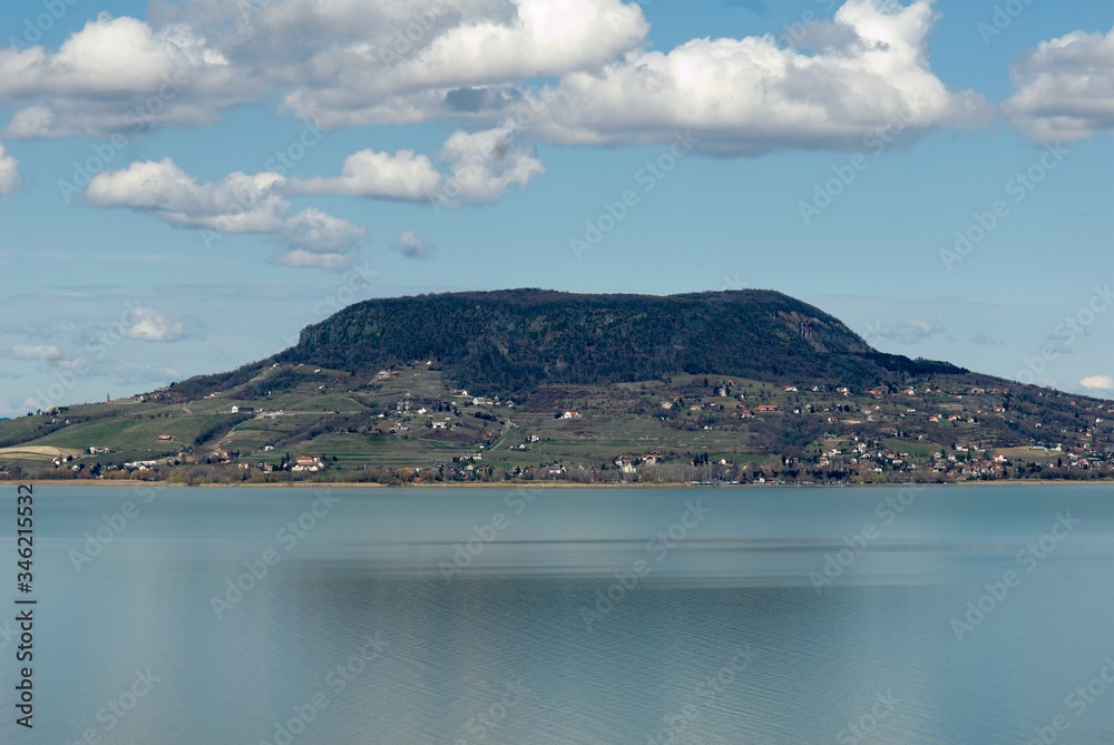 Lake Balaton is the largest lake in Hungary and Central Europe, on the other side is the Badacsony volcano. On the shore trees without leaves in autumn, blue sky and clouds, panoramic shot.