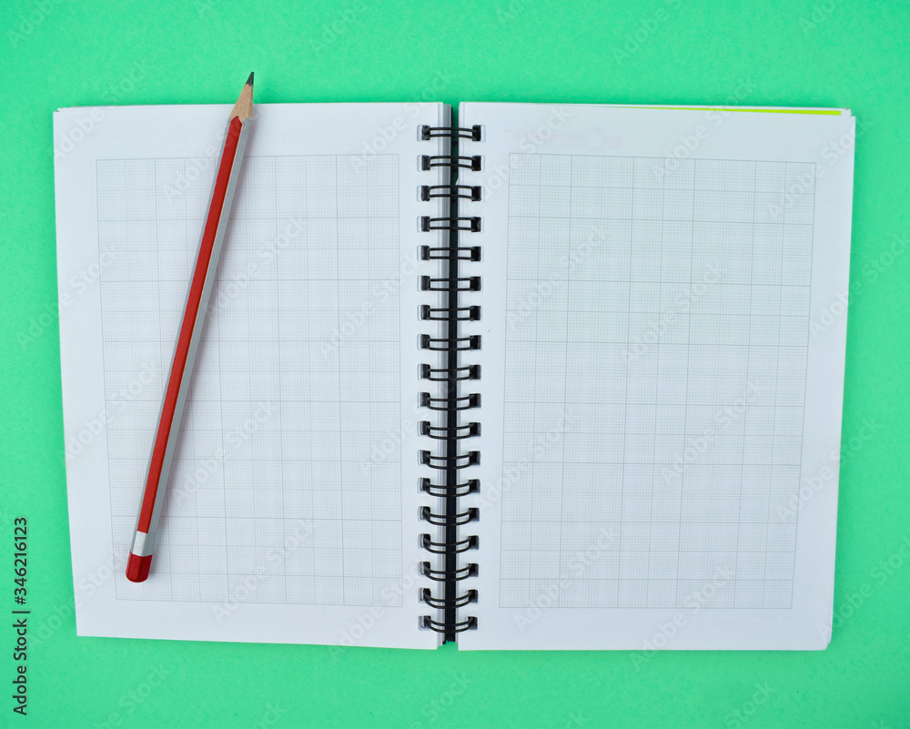 Red colored wood pencil crayon placed on top of a white spiral note book Red colored wood pencil crayon placed on top of a white spiral note book