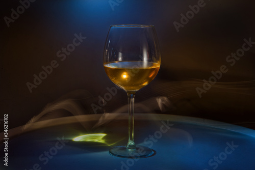White wine in a glass on the table on a creative black background. Cigarette smoke in the bar and an alcoholic drink at a party or disco. Shooting in the dark key. Copy space.