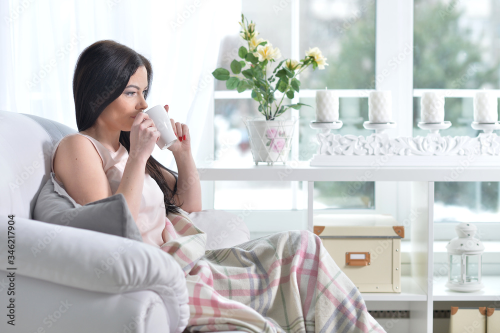 Young woman sitting in armchair and drinking tea at light room Young woman sitting in armchair and drinking tea at light room