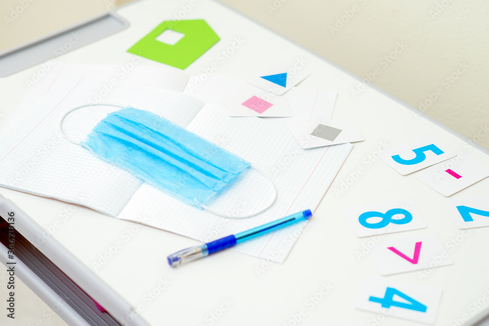 Medical mask with pen over copybook next to numbers on the desk. Quarantined school concept. Medical mask with pen over copybook next to numbers on the desk. Quarantined school concept.