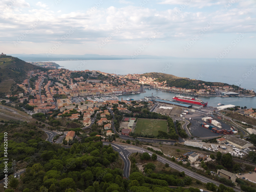 Shot from drone. European city on the sea coast among the mountains and roads of the serpentine. Sea port city on the ocean. A large red cruise ship in the city's seaport, surrounded by small houses