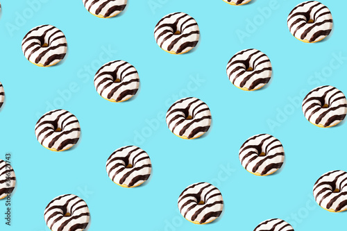 Pattern made of glazed donut on blue background. Party food concept with copy space. Top view.