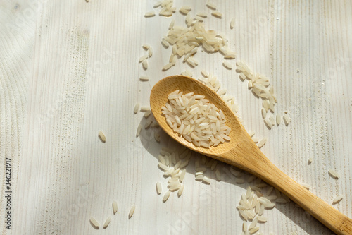 Aerial view of wooden spoon with raw white rice, on white wooden table, horizontal, with copy space