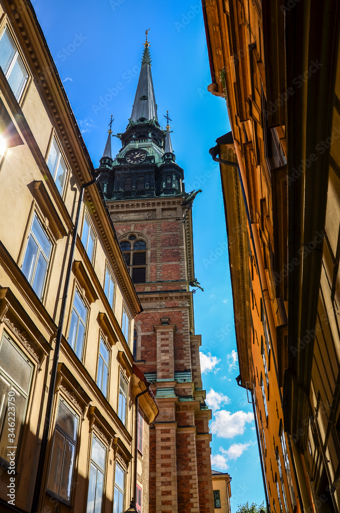 Fototapeta premium Low angle view on of facades of houses and the bell tower of the German church at old street in Gamla Stan in Stockholm, Sweden