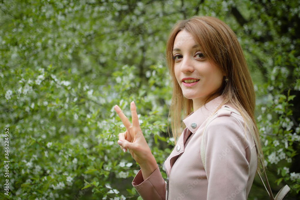 Blonde woman is showing victory on flowering tree background in the garden during early spring. Allergy concept Blonde woman is showing victory on flowering tree background in the garden during early spring. Allergy concept