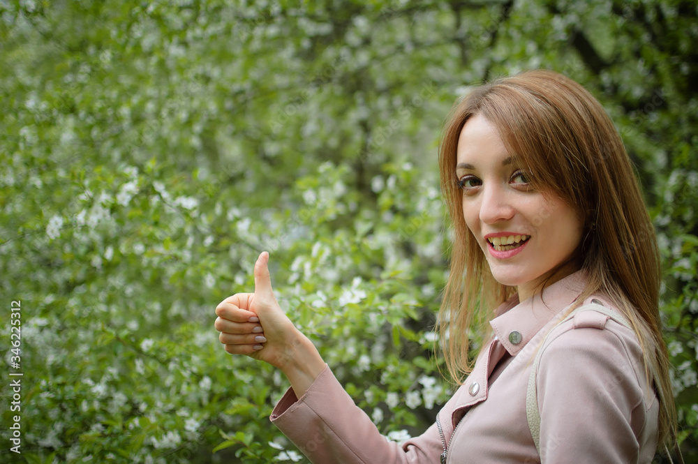 Blonde woman is showing thumb on flowering tree background in the garden during early spring. Stop allergy concept Blonde woman is showing thumb on flowering tree background in the garden during early spring. Stop allergy concept