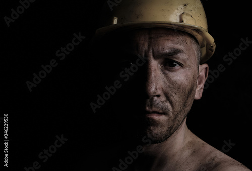 Fotografía Miner in a yellow hard hat on a black background dirty with coal dust